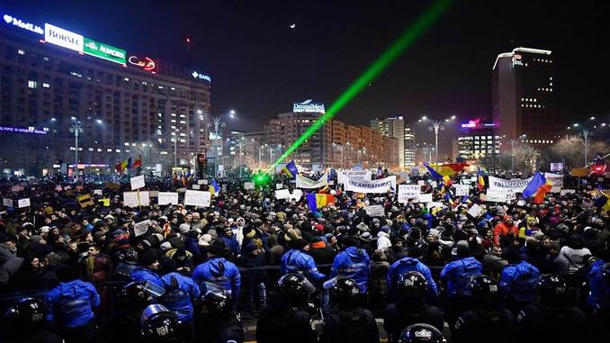 Romanian riot police stand guard as people demonstrate against controversial decrees to pardon corrupt politicians